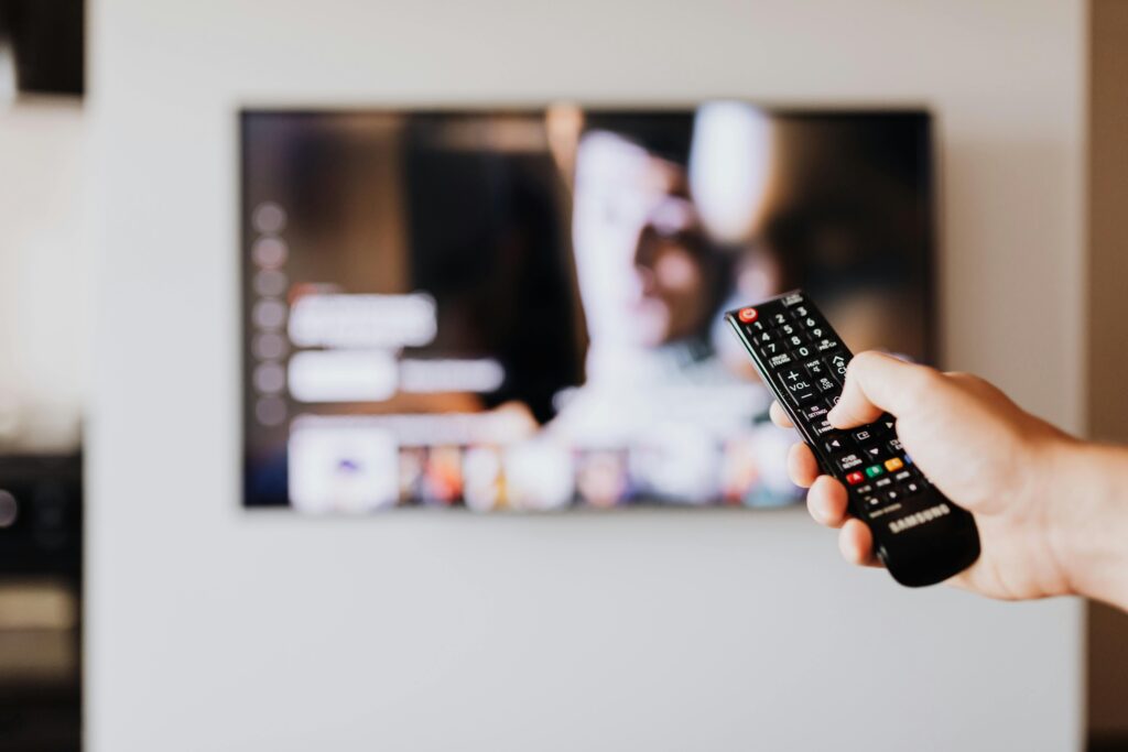 A young boy with a remote control, engaged in finding TV alternatives to live NYT news on a blurred TV screen.